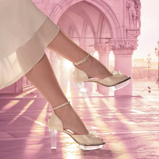 Ein zauberhafter Brautschuh als Opentoe Riemchenpump von der Firma Cinderella’s by Marcela in Ivory/Perlfarbe mit elegantem Nuss-Logo (als Inspiration aus dem Märchen drei Nüsse für Aschenbrödel) sowie hochwertigem transparenten Absatz und Plateau. Die Schuhe sind mit silbernen Accessoires verziert, und die Schnalle ist mit funkelnden Steinchen veredelt. Perfekt geeignet für Hochzeiten sowie alle gehobene Events. Im Hintergrund ist Venedig.