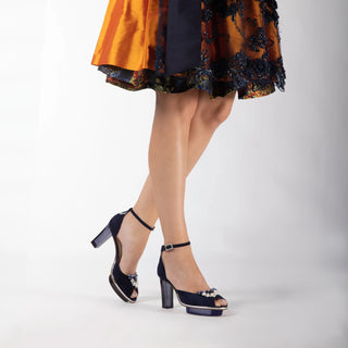 Ein magischer nachtblauer Peeptoes Riemchenpump von der Firma Cinderella’s by Marcela aus Wildleder mit elegantem Nuss-Logo (als Inspiration aus dem Märchen drei Nüsse für Aschenbrödel) sowie hochwertigem transparenten Absatz und Plateau. Die Schuhe sind mit silbernen Accessoires verziert, und die Schnalle ist mit funkelnden Steinchen veredelt. Perfekt geeignet für Abendmode, gehobene Events, Trachtenevents aber auch im Business-Outfit.