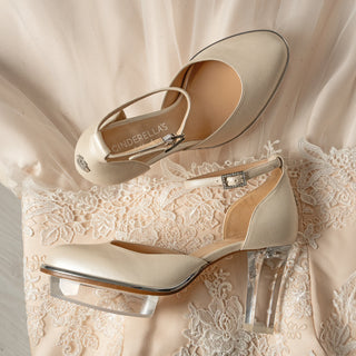 Ein zauberhafter bequemer Brautschuh als Closetoe Riemchenpump von der Firma Cinderella’s by Marcela in Ivory/Perlfarbe mit elegantem Nuss-Logo (als Inspiration aus dem Märchen drei Nüsse für Aschenbrödel) sowie hochwertigem transparenten Absatz und Plateau. Die Schuhe sind mit silbernen Accessoires verziert, und die Schnalle ist mit funkelnden Steinchen veredelt. Perfekt geeignet für Hochzeiten sowie alle gehobene Events.