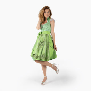 Eine Frau posiert in einem grünen Dirndl (Kleid) von Astrid Söll mit Brautschuhen von Cinderellas_by_Marcela in ivory-Farbe und hellgrüner Brosche in einem Fotostudio.