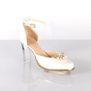 Ein zauberhafter Brautschuh als Closetoes Riemchenpump von der Firma Cinderella’s by Marcela in Ivory/Perlfarbe mit elegantem Nuss-Logo (als Inspiration aus dem Märchen drei Nüsse für Aschenbrödel) sowie hochwertigem transparenten Absatz und Plateau. Die Schuhe sind mit goldenen Accessoires verziert, und die Schnalle ist mit funkelnden Steinchen veredelt. Perfekt geeignet für Hochzeiten sowie alle gehobene Events.