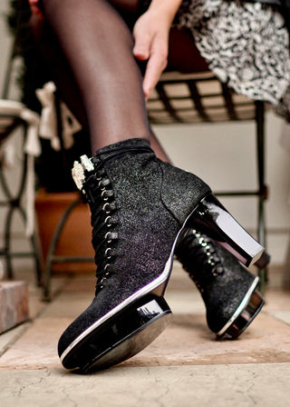 Frauenfuß in schwarzen Stiefeletten aus Leder mit transparentem Absatz und Kristallschmuck