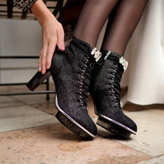 Frauenfüße in schwarzen Stiefeletten mit Schmürchen aus Leder mit transparentem Absatz und Kristallschmuck