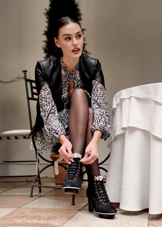 Frau in schwarzen Stiefeletten aus Leder mit transparentem Absatz und Kristallschmuck